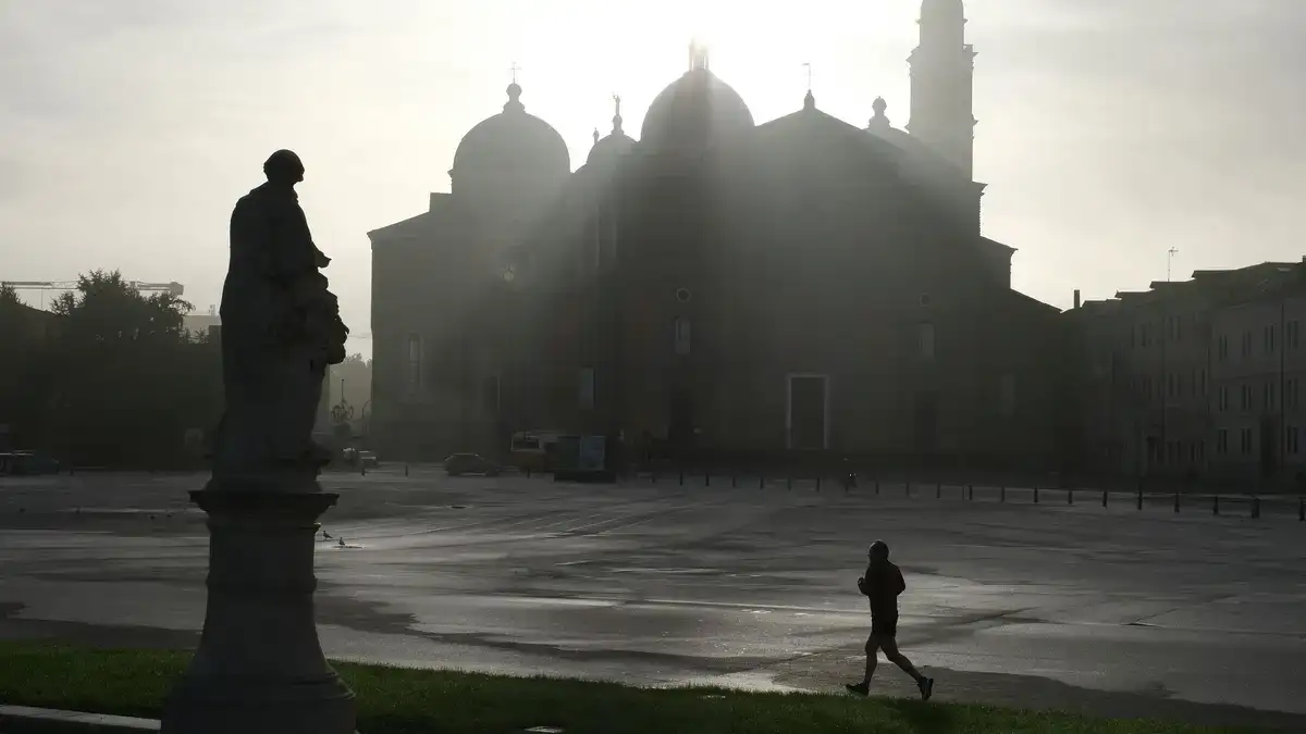 A jogger silhouettes against a misty European piazza with a historic church at sunrise.